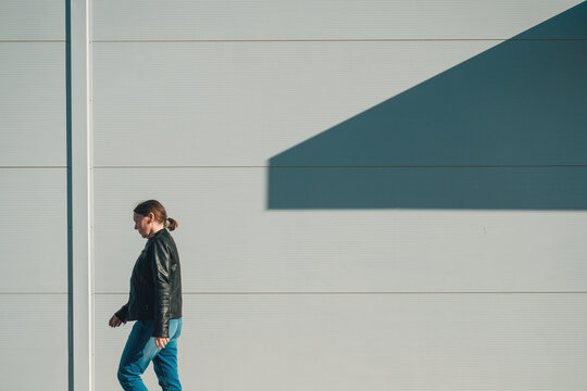 Woman walking along minimal urban wall with geometric shadow in casual leather jacket