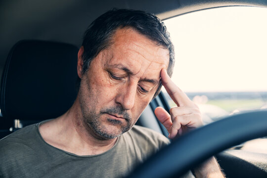 Mature man inside vehicle looking down with furrowed brows and tired eyes, anxiety and concern concept
