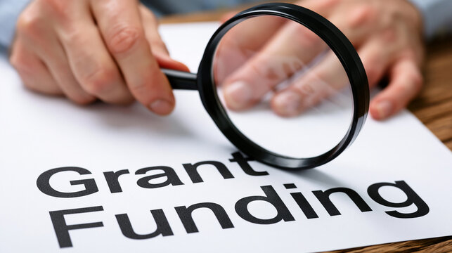 A person examines grant funding opportunities with a magnifying glass closely.