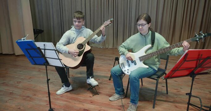 Boy and Girl Practice Playing Music on Stage. Kids Play Guitar and Bass Guitar. 4K 10-bit
