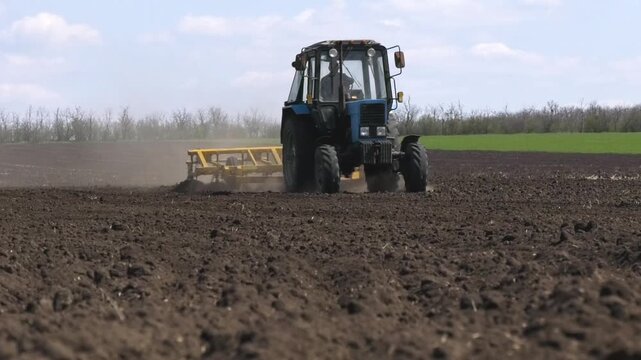 Tractor with a seeder driving through a plowed field in spring. Green winter wheat is visible in the background. Concept of seasonal agricultural work, sowing campaign, soil cultivation, and modern