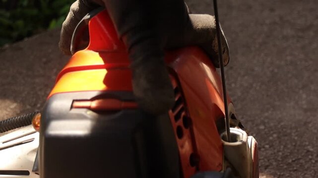 Outdoor close up of gloved hands pulling the starter rope on a grass trimmer engine before cutting grass, highlighting recoil starter details and lawn care equipment in daylight.