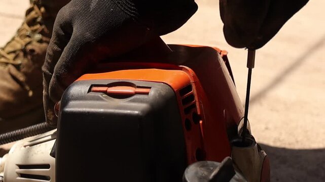 Detailed video of a person starting a fuel powered grass trimmer by pulling the recoil starter rope, with focus on engine housing, gloved hands and lawn maintenance preparation outdoors.