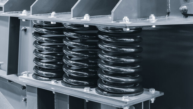 Blue industrial metal structure features three black coil springs. Stainless steel bolts secure the springs to the frame. The setup suggests mechanical or electrical equipment use
