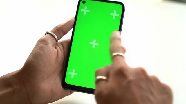 An extreme close-up, eye-level, static video shows human hands holding a modern smartphone with a vibrant chroma key screen and tracking markers, indoor setting, clean, professional product