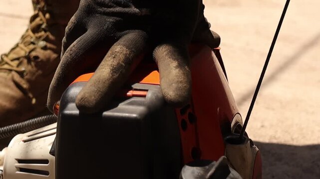 Close up video of hands pulling the starter cord on a gasoline grass trimmer before yard work, showing engine details, recoil mechanism and protective gloves during outdoor lawn care.