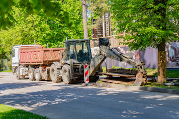 Backhoe loader with specialized machinery working on urban infrastructure development and residential construction project near roadside area © K