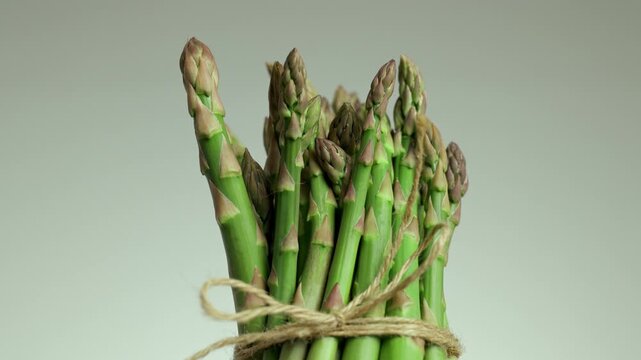 Healthy bunch of raw green asparagus tied with twine rotating and spinning to display the healthy edible shoots on a light background