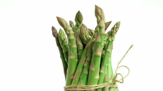Bunch of raw green asparagus tied with twine rotating and spinning displaying the edible shoots on a white background