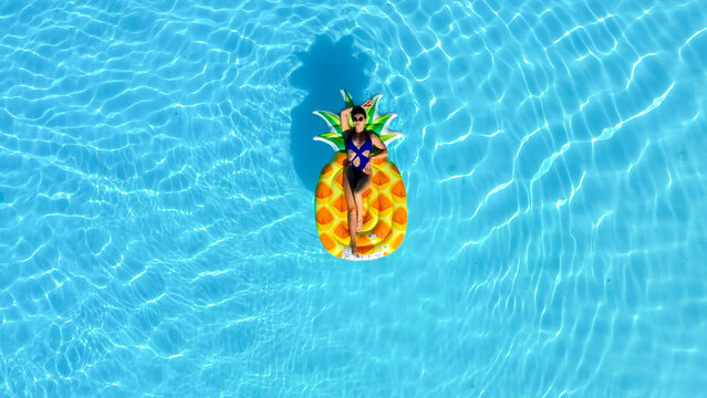 Aerial drone shot of woman floating on inflatable mattress in outdoor swimming pool. Concept summer vacation, relaxation and luxury lifestyle.

