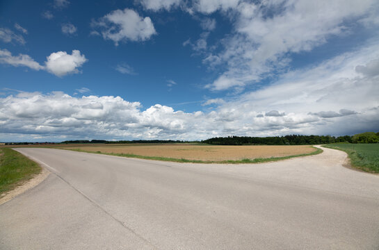 A road splits into two roads. Above the roads is a blue sky with clouds.