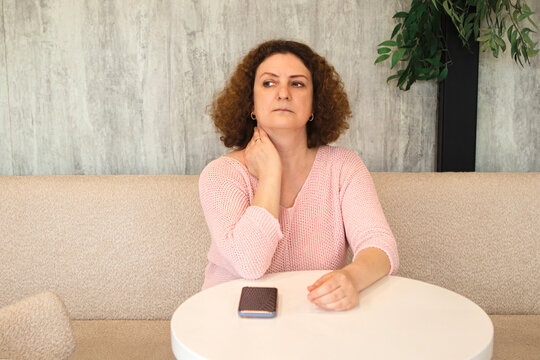 Middle-aged woman sitting at a table looking thoughtful and waiting with phone in front of her