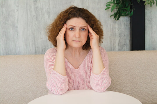 Woman holding her temples with headache and stress while sitting at a table in a living room
