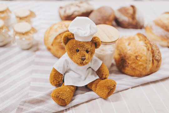 Baker bear prepares various types of sourdough bread and dough in a bakery setting with fresh ingredients on the table