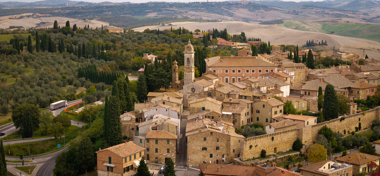 Aerial drone view of San Quirico d'Orcia borgo with red tile roofs. Panoramic view of historic Tuscan village with rolling hills background of Val d'Orcia valley, Italy.  countryside of Tuscany