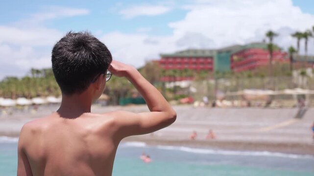 Young vacation traveler standing by sea and looking at tropical coastline on summer holiday. Teen tourist enjoying sea view from pier on summer vacation. Summer holidays concept.