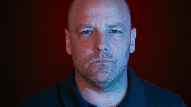 Middle-aged bald white man side profile and turning head to face the camera, staring intensely. 