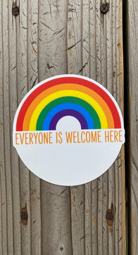 Rainbow sticker with text "Everyone Is Welcome Here" on rustic wooden planks, symbolizing inclusivity, acceptance, and diversity