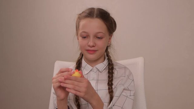 Young girl engages with rubber duck. Closeup of girl nudging toy duck on table surface. Young girl delicately presses rubber duck with braided hair for playful interaction