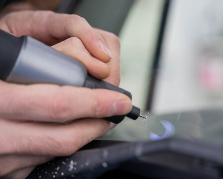 A technician drills a hole during a car windshield chip repair.