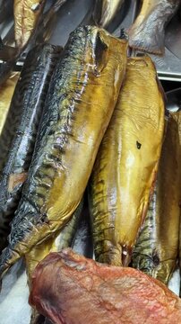 Close-up smoked mackerel fillets on counter, arranged in neat rows at artisan fish stall, glistening oily skin with striped