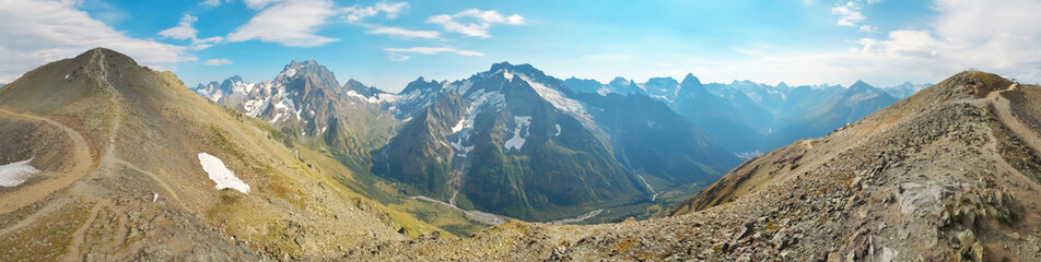 Fototapeta premium Wide Panoramic View of Snowy Mountain Peaks in Dombay Caucasus with Blue Sky