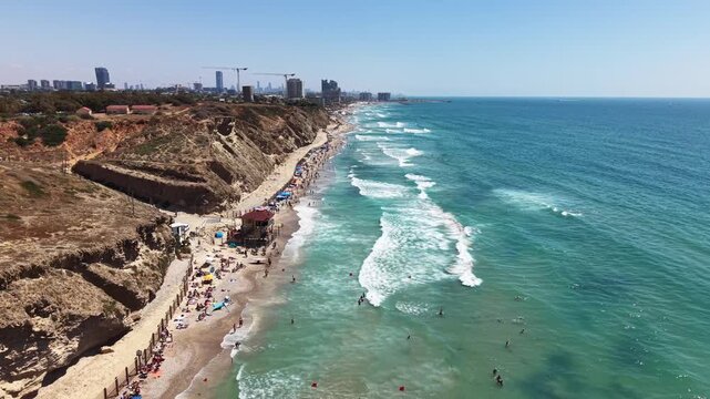 Aerial drone view of Sidna Ali Beach with sandy shore, turquoise waves, sandstone cliffs and city skyline in Israel
