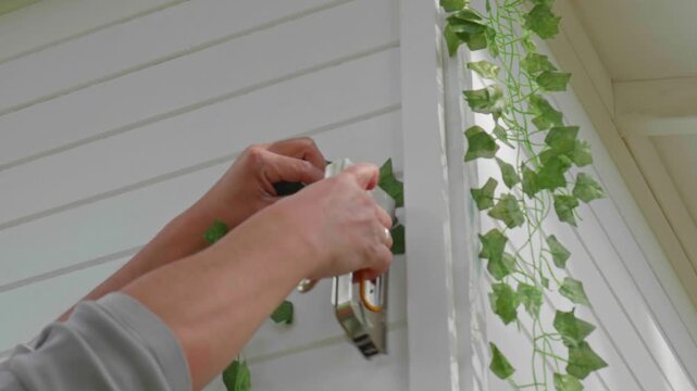 Stapling Artificial Ivy Plant onto White Wooden Wall for Interior Decor