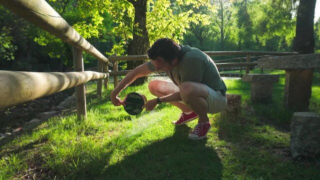 Man Pours Water from Pot onto Lush Green Grass in Sunny Park