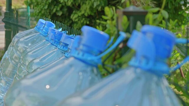 Row of Empty Large Plastic Water Bottles with Blue Caps on Wire Fence