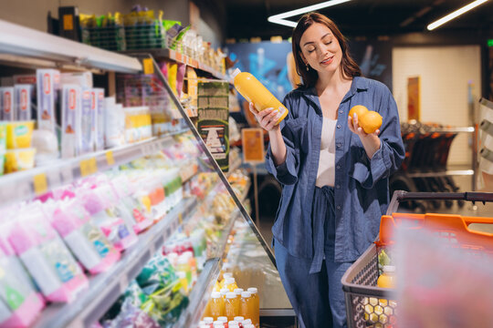 Woman choosing fresh orange juice and fruit comparing healthy beverage with natural citrus in supermarket aisle