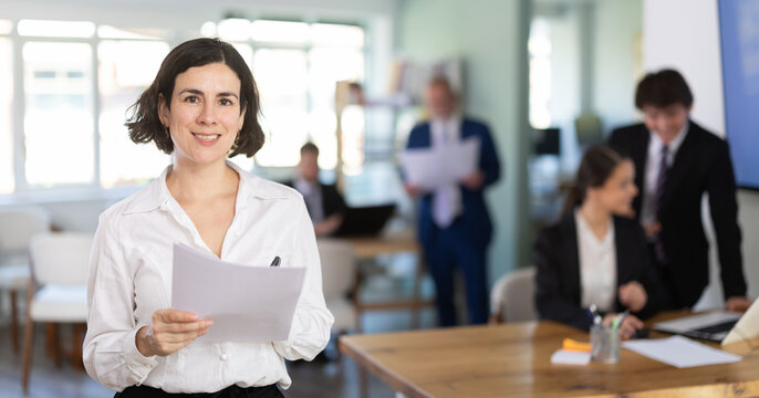 Woman stands against the background of the interior of a modern office and holds documents, she solves work problems. European woman gets a job in a company and holds a resume in her hands
