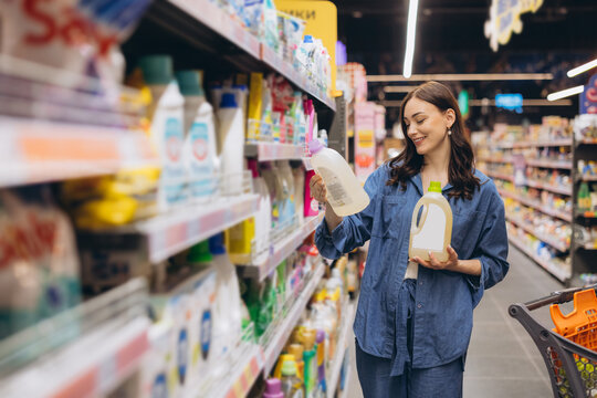 Woman choosing liquid detergent in supermarket, comparing products and shopping for household supplies