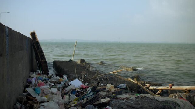 Plastic waste and scattered litter covering coastal rocks along an urban shoreline, highlighting marine pollution and environmental damage in ocean ecosystems.