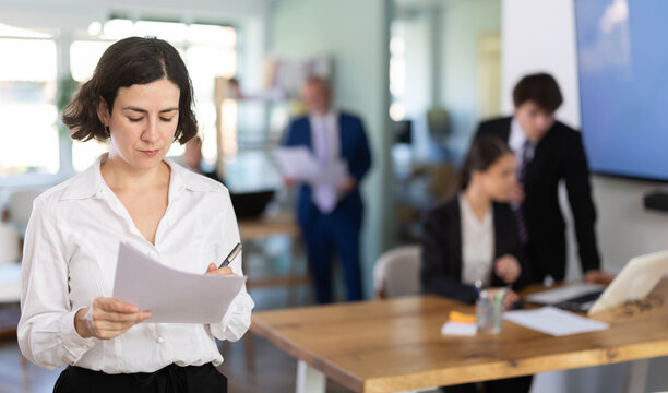Woman stands against the background of the interior of a modern office and holds documents, she solves work problems. European woman gets a job in a company and holds a resume in her hands