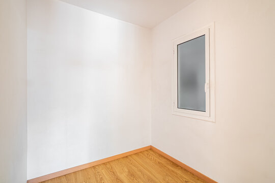 Empty room with white walls and a wooden floor. A single window is present, allowing natural light to enter the space