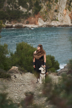 A woman walks with a Siberian Husky dog near the sea. Natural scenery with cliffs water and soft daylight creates authentic travel lifestyle feeling outdoors.