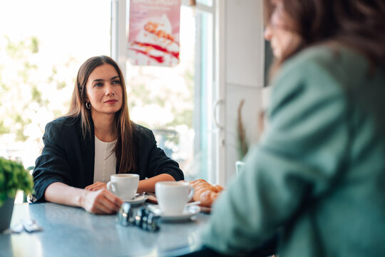 Two professional women enjoying a relaxed coffee chat in a modern cafe, smiling and discussing work and friendship during a break