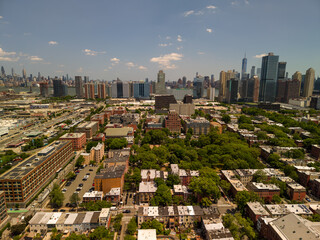 Fototapeta premium Aerial view of jersey city residential neighborhoods, parks and roads leading toward the distant new york city skyline and one world trade center across the hudson river during daytime
