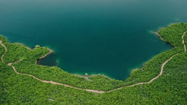 Slansko Lake, Montenegro - 05 29 2025: Top-down still drone video of Slansko Lake in Ponikvica, showing teal water, dense forest shoreline, winding path, and tranquil scenery under cloudy skies.