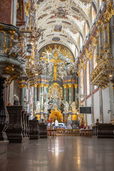Fototapeta premium Magnificent baroque church interior with richly decorated ceiling, golden altar, frescoes and ornate sculptures. Historic Catholic architecture in Poland with luxurious sacred design.