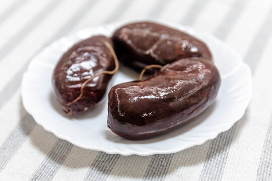 Three traditional blood sausages (morcela, chouri&ccedil;o) served on a white plate over a striped tablecloth.
