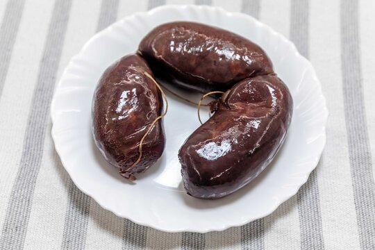 Three traditional blood sausages (morcela, chouri&ccedil;o) served on a white plate over a striped tablecloth.