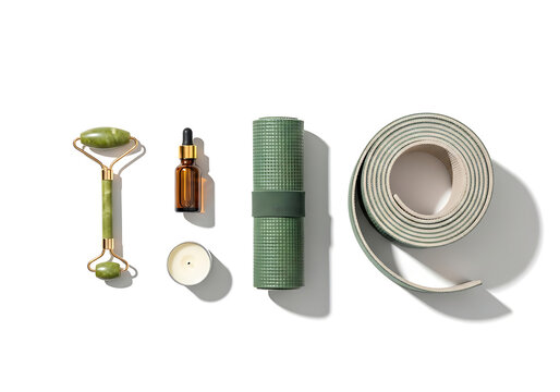 Green jade facial roller essential oil bottle candle and rolled yoga mat on white background
