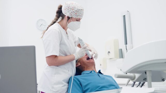 Professional female dentist using an intraoral 3d scanner on a male patient for a digital impression of teeth in a modern dental clinic