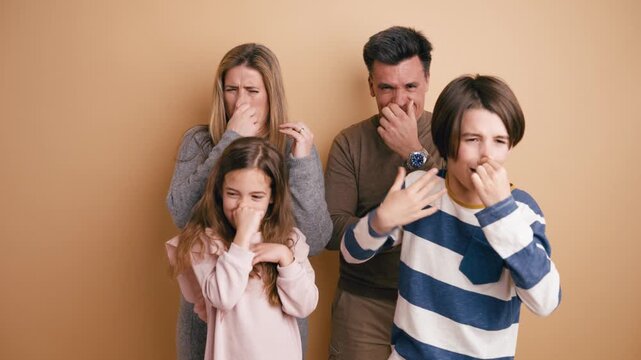 Family of four with two children reacting to a bad smell. Parents and kids plugging their noses and showing disgusted facial expressions