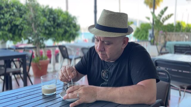 Hombre removiendo az&uacute;car en caf&eacute; en terraza del paseo mar&iacute;timo