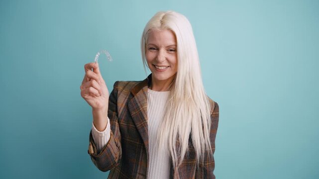 Smiling happy woman showing a removable transparent aligner for dental correction. Orthodontic treatment and invisible braces concept