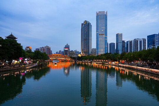 Wide angle view of Jin River reflecting modern skyscrapers and illuminated Anshun Bridge at twilight, Chengdu, Sichuan, China