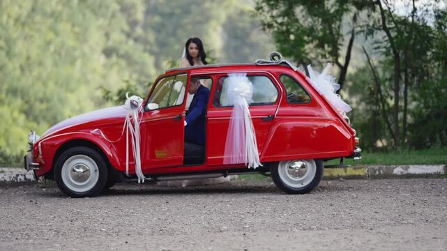 Couple exit out of vintage red convertible car adorned with wedding ribbons